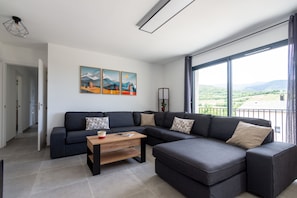 A modern living room with a sectional sofa, a wooden coffee table, and a large window offering a view of the countryside. - L’Échappée Cerdane - Jolie maison pyrénéenne (Saillagouse)