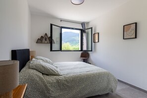 A bedroom with a bed, a window, a lamp, and a wall-mounted shelf. - L’Échappée Cerdane - Jolie maison pyrénéenne (Saillagouse)