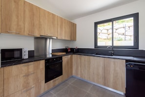 A modern kitchen with wooden cabinets, a microwave, a stove, and a dishwasher. - L’Échappée Cerdane - Jolie maison pyrénéenne (Saillagouse)