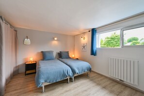 Ein Schlafzimmer mit zwei Betten, Nachttischlampen, einem Fenster mit Vorhängen, einer Heizung und einer Meeressterne als Dekoration.