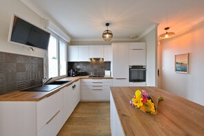 Eine moderne Küche mit weißen Schränken, einer Holz Arbeitsplatte, einem eingebauten Ofen und einem großen Fenster.