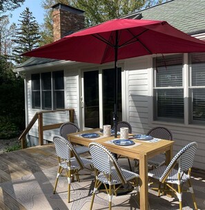 An outdoor dining area with a wooden table and chairs, a red umbrella, and a brick chimney in the background. - Relax in Blue Haven, a cozy 2-bedroom home in Southport, ME, perfect for 2-4 guests. (Southport)