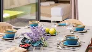 A dining table set with blue bowls, plates, and glasses, with a bed visible through a window in the background. - Villa Camarines, new villa, pool, walk to beach (Agde)