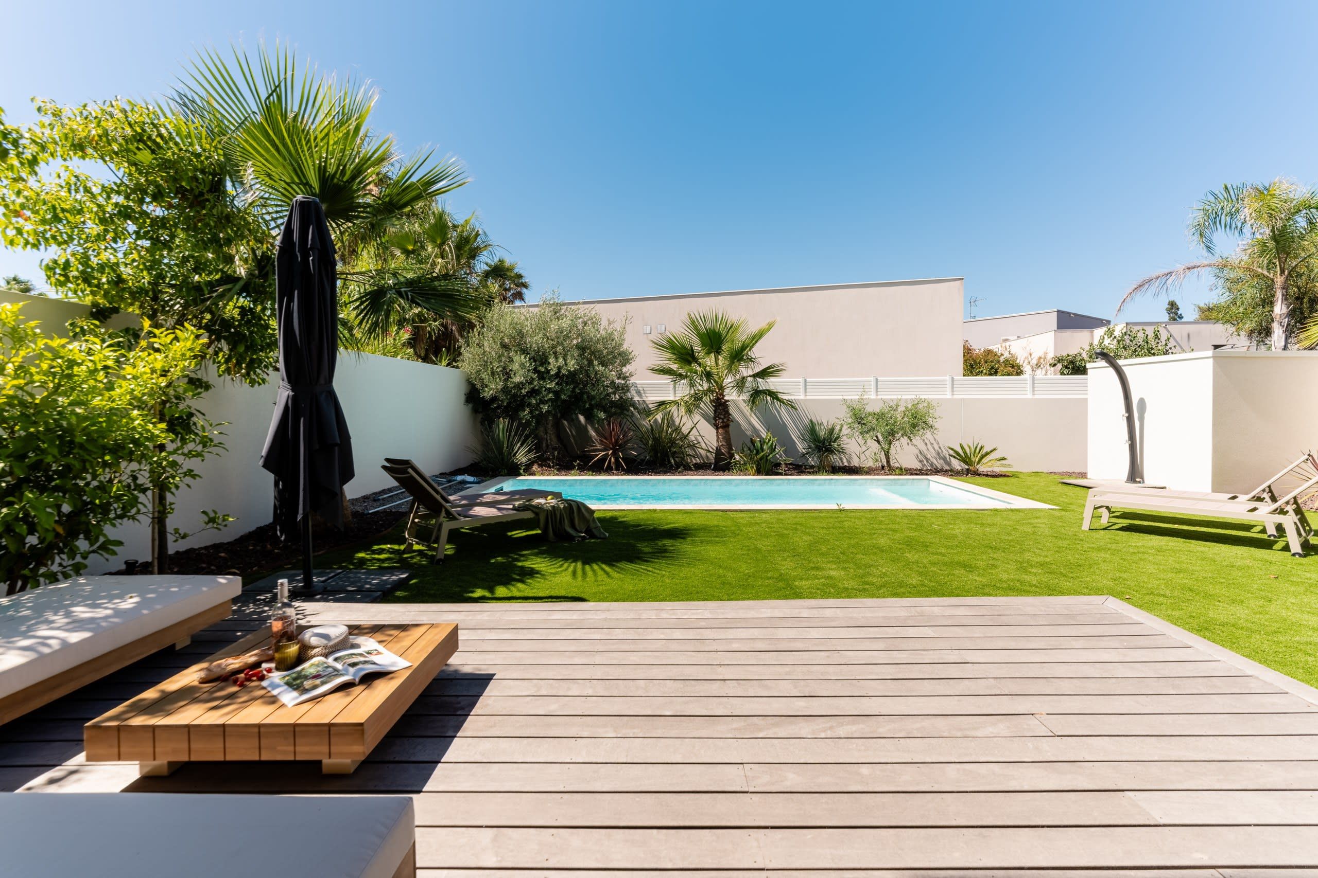 Um quintal com piscina, deck de madeira e área de estar com cadeiras e mesa.