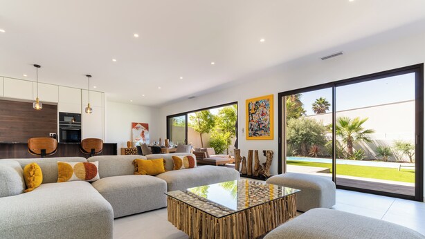A modern living room with a sectional sofa, a glass coffee table, and a view of the outdoors. - Villa Camarines, new villa, pool, walk to beach (Agde)