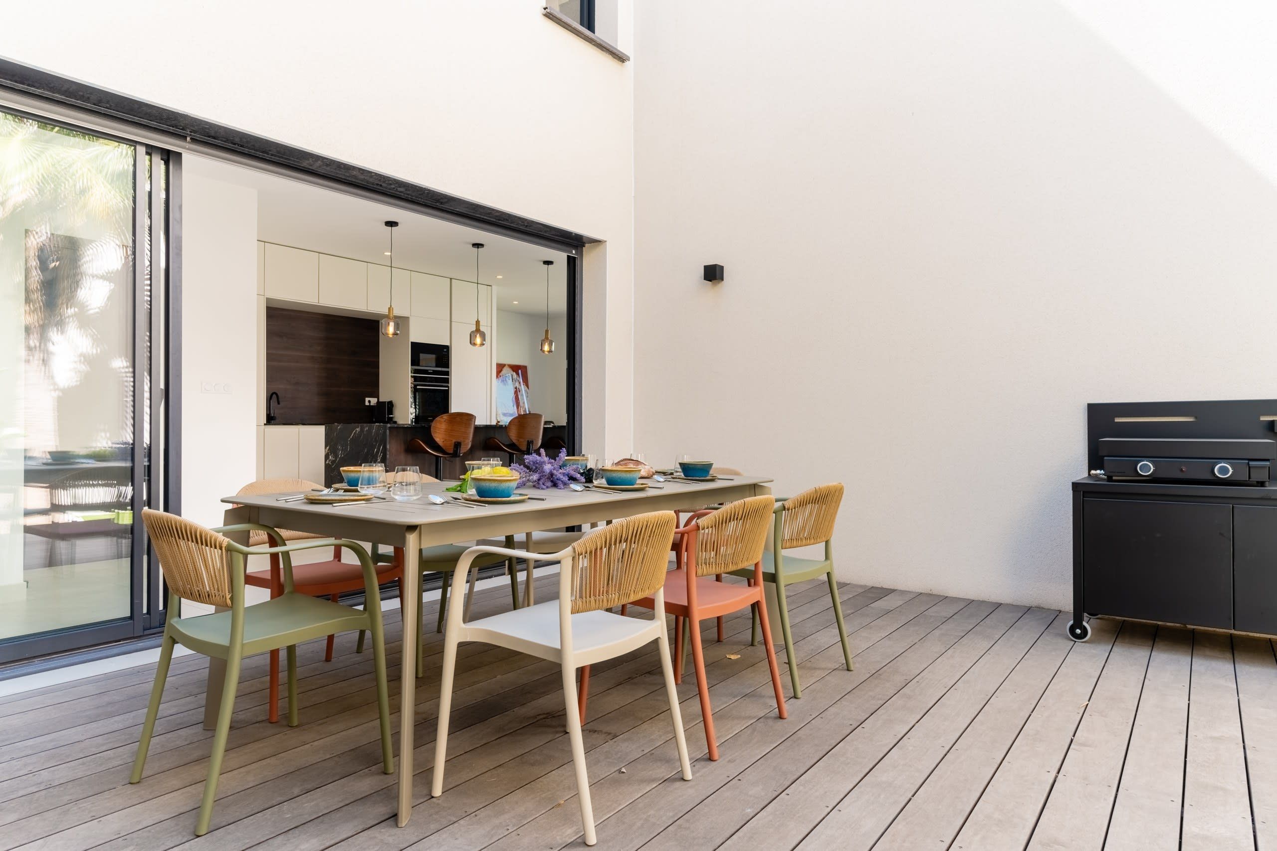 Un espace extérieur aménagé pour les repas, avec une table dressée pour quatre personnes, entourée de chaises en osier, et un barbecue placé sur le côté.