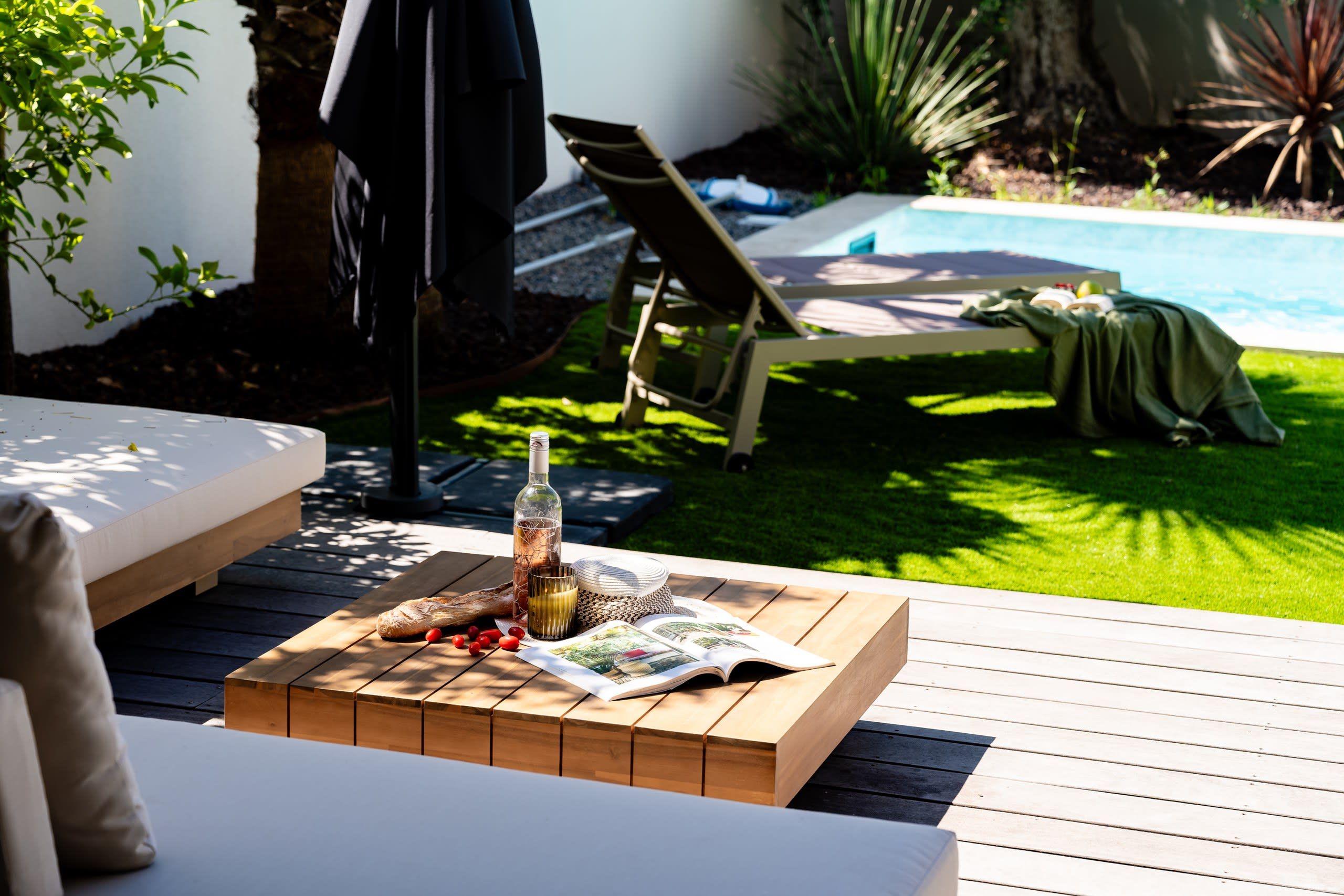 Una terraza de madera con una mesa dispuesta para una comida, una botella y un libro.