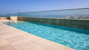 A rooftop swimming pool with clear blue water, a glass barrier, and a cityscape view in the background. - Caribbean Mist by Hilal - Wifi - Seaview - Beach (Cartagena)