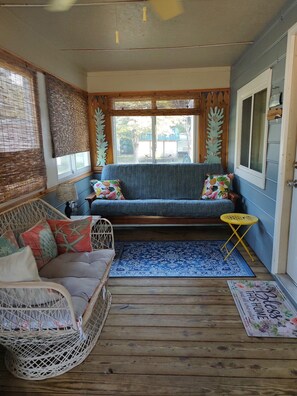 Una habitación acogedora con un sofá azul, una silla de mimbre y una pequeña mesa amarilla.