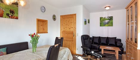 A room with a dining table, chairs, a sofa, a cabinet, and a wall clock.