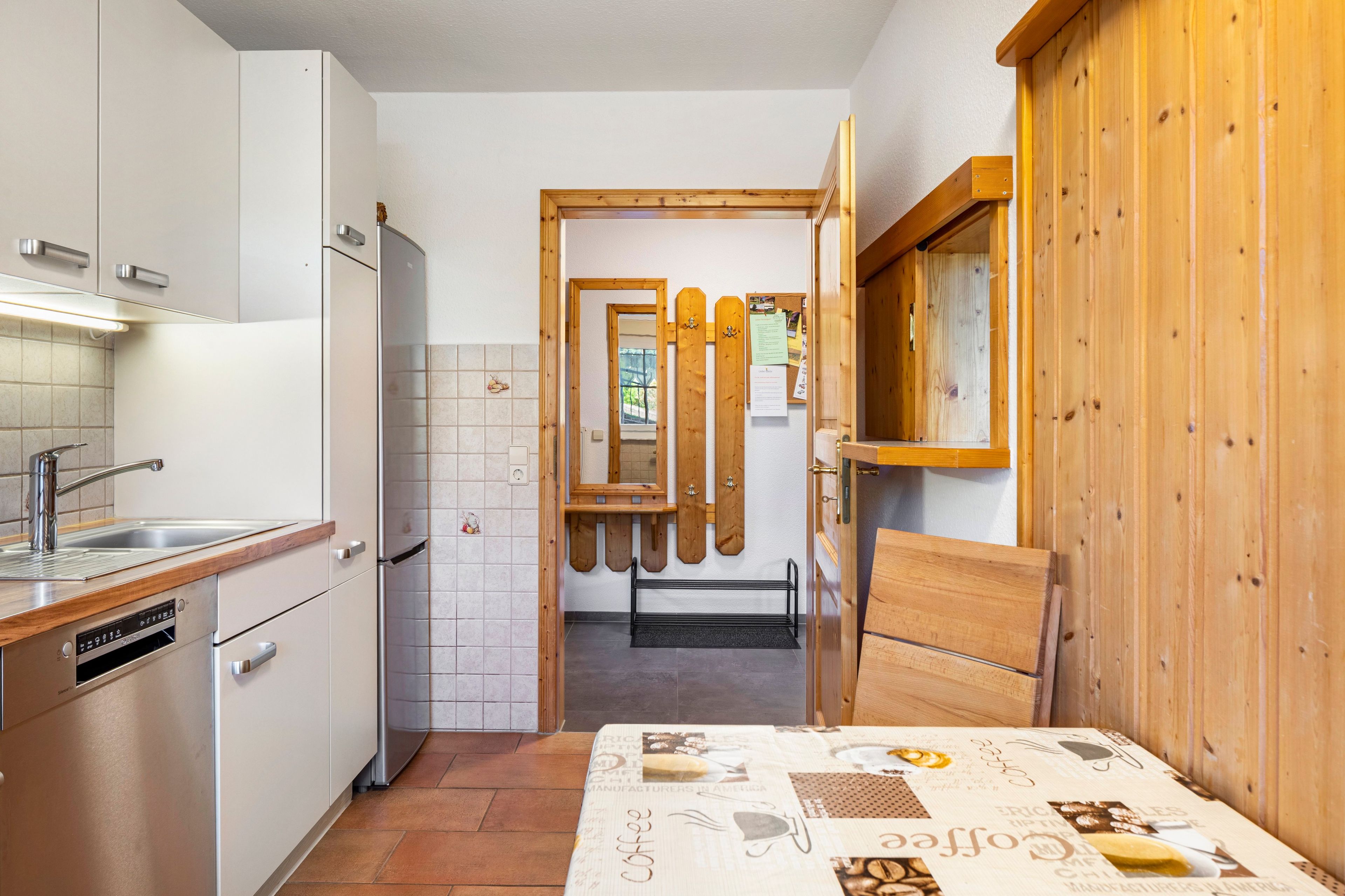 Una cocina con armarios blancos, un lavamanos de acero inoxidable y una puerta de madera que da a otra habitación.