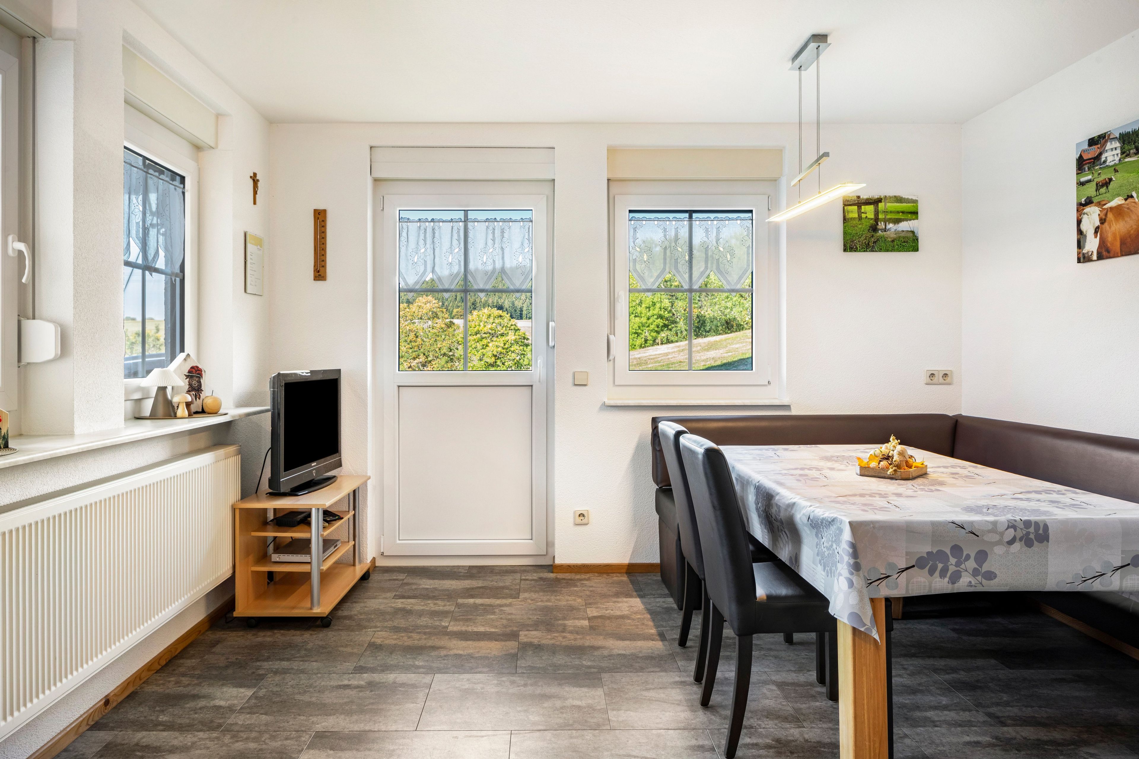 A compact living space with a dining area, a television on a wooden stand, and a view of greenery through the windows.