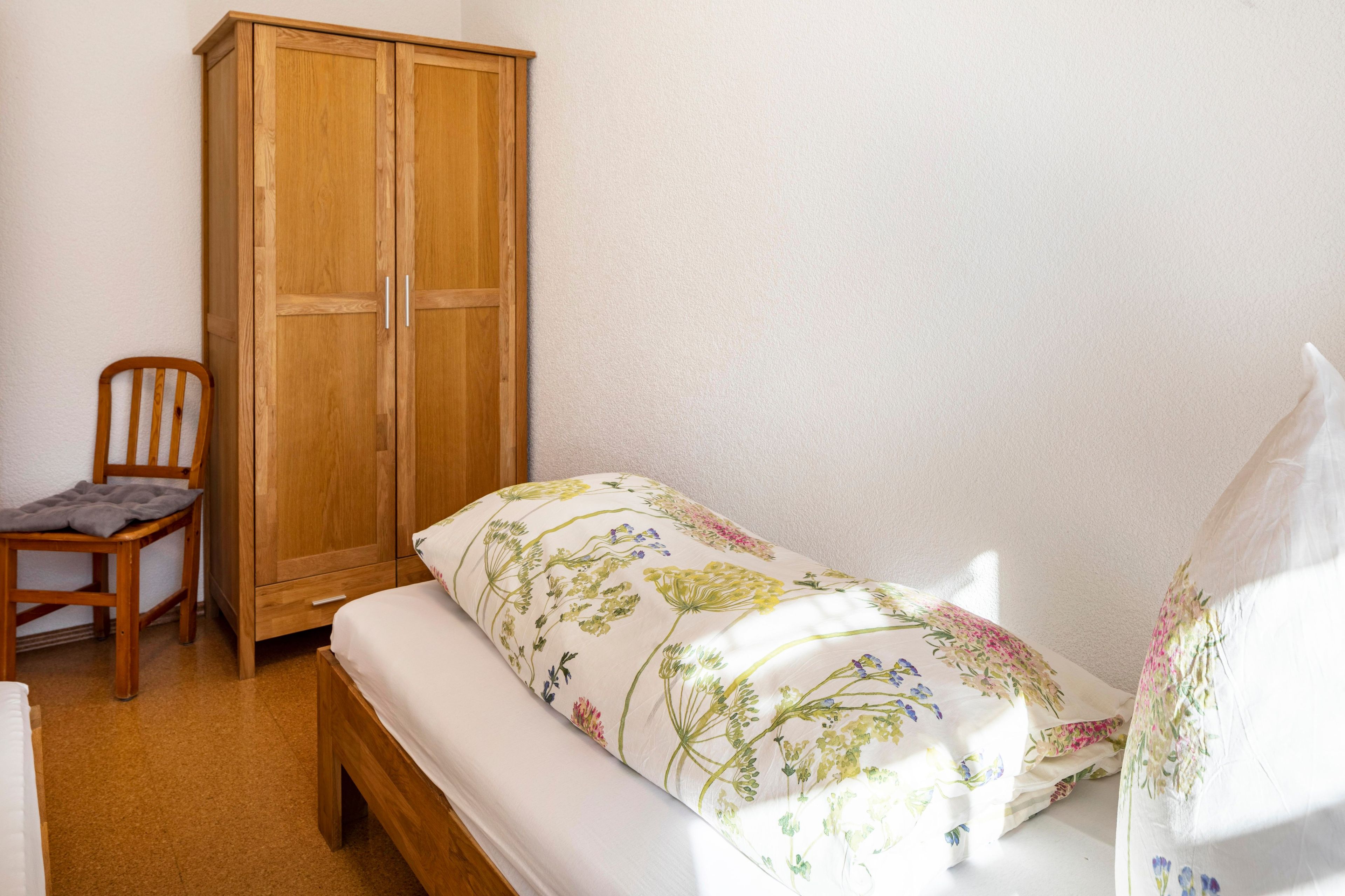 Habitación pequeña con cama individual, armario de madera y una silla.