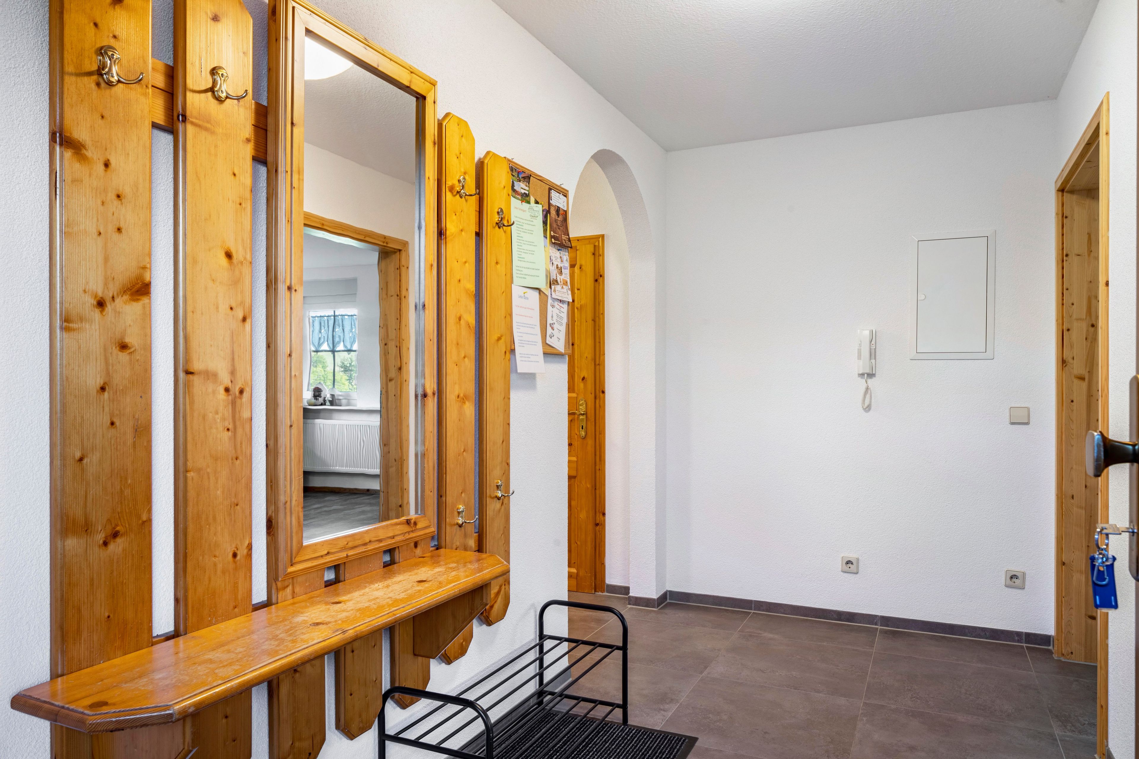 Un couloir avec des portes en bois, un banc, un miroir et un téléphone fixé au mur.
