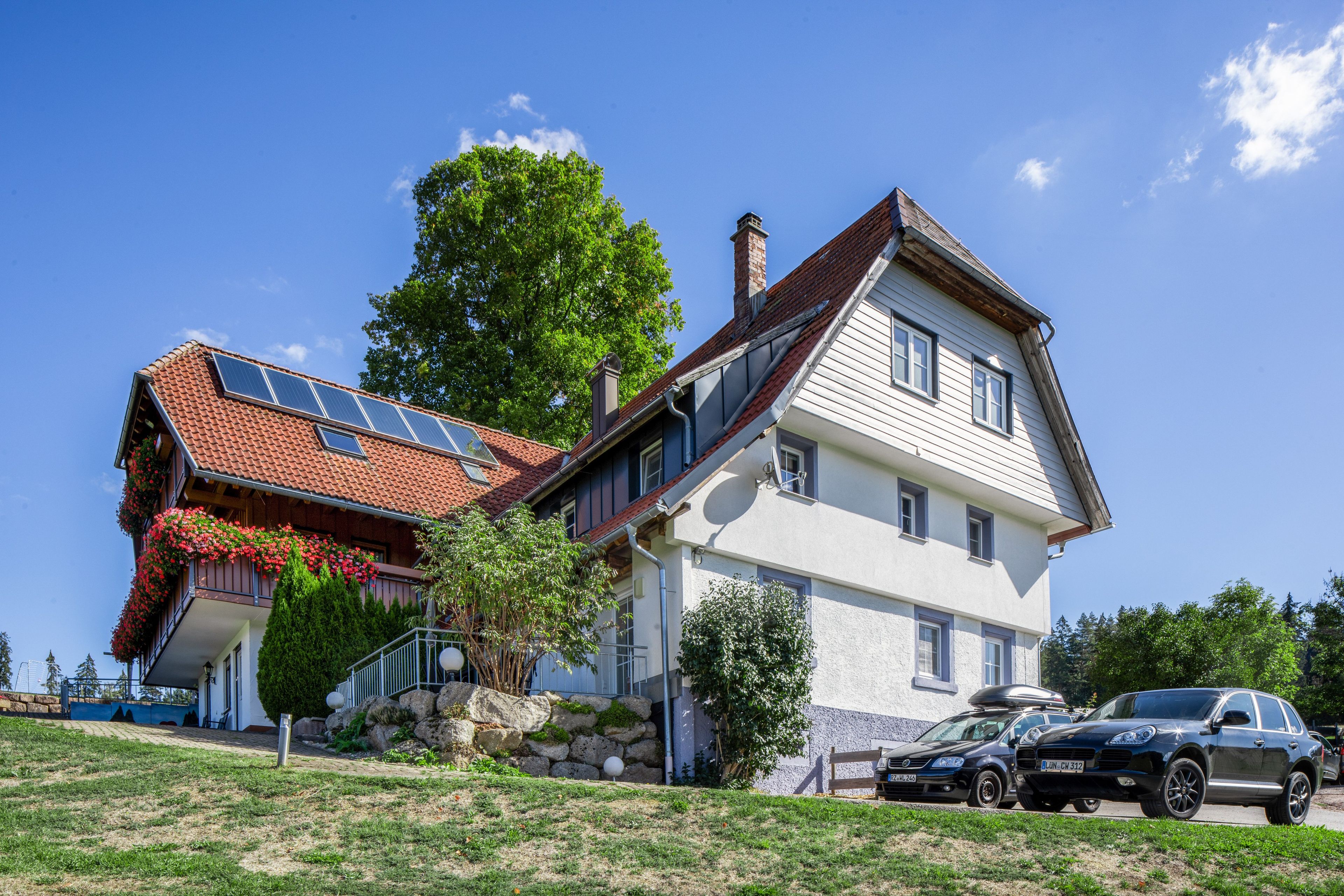Ein zweistöckiges Haus mit geneigtem Dach, Solaranlagen und einem Auto auf der Auffahrt.