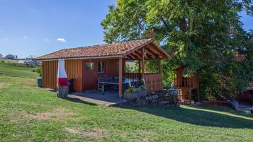 A wooden cabin with a tiled roof, a patio with outdoor seating, and a stone wall.