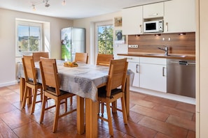 A modern kitchen with a dining area, featuring a table with chairs, a refrigerator, a microwave, and a dishwasher. - Apartment 'Sonnenstrahl' on the Farm with Terrace, Barbecue, Playground and Green View (Sankt Georgen im Schwarzwald)