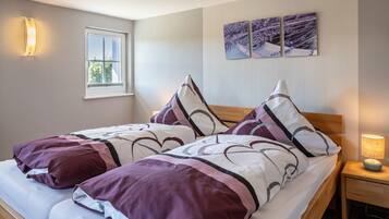 A neatly made bed with patterned bedding, a bedside lamp, and a window with blinds.