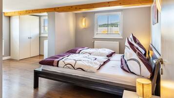 A bedroom with a bed, wooden floor, a window with a view, and a bedside lamp.
