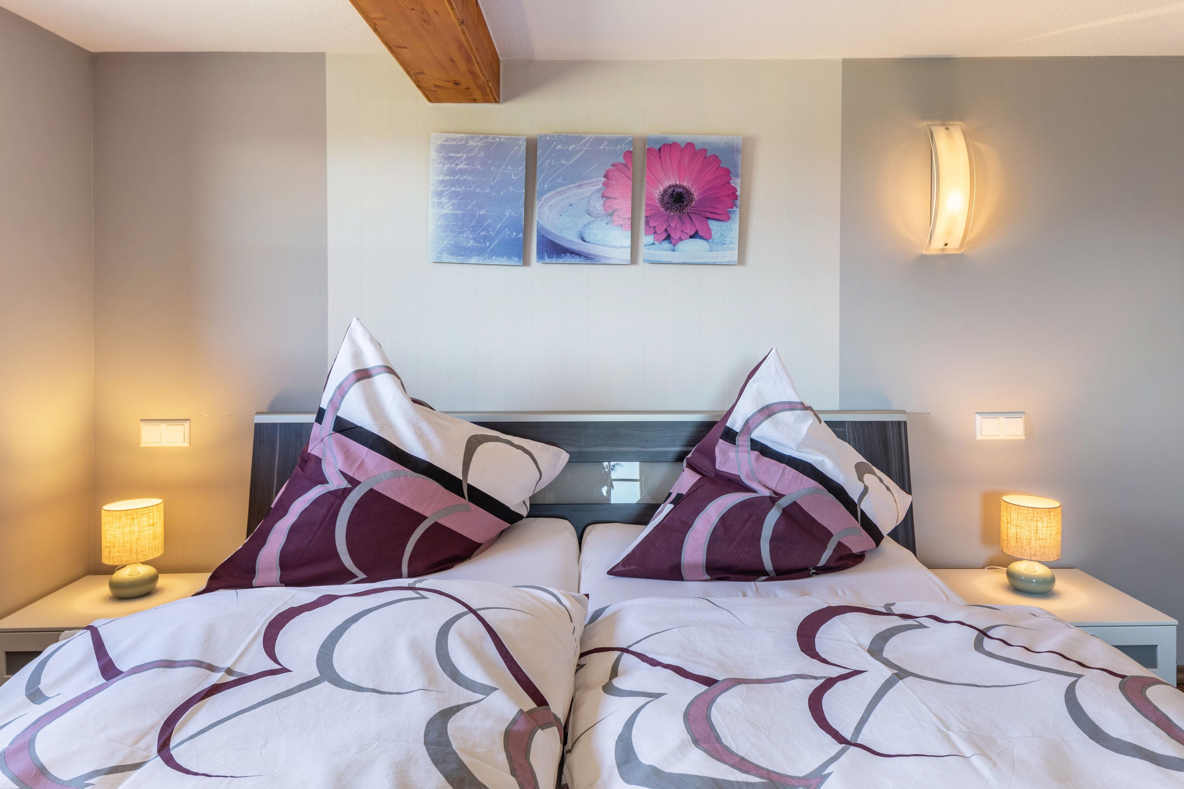 A hotel room with two beds, each with a headboard, and two bedside lamps. There are two wall-mounted artworks above the beds.