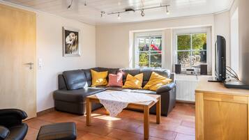 A living room with a sofa, a coffee table, a TV, and a window with a view of a garden.