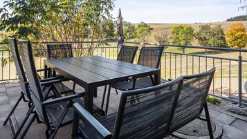 An outdoor patio with a table and chairs, surrounded by a metal railing, overlooking a rural landscape.