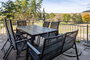 An outdoor patio with a table and chairs, surrounded by a metal railing, overlooking a rural landscape. - Apartment 'Sonnenstrahl' on the Farm with Terrace, Barbecue, Playground and Green View (Sankt Georgen im Schwarzwald)