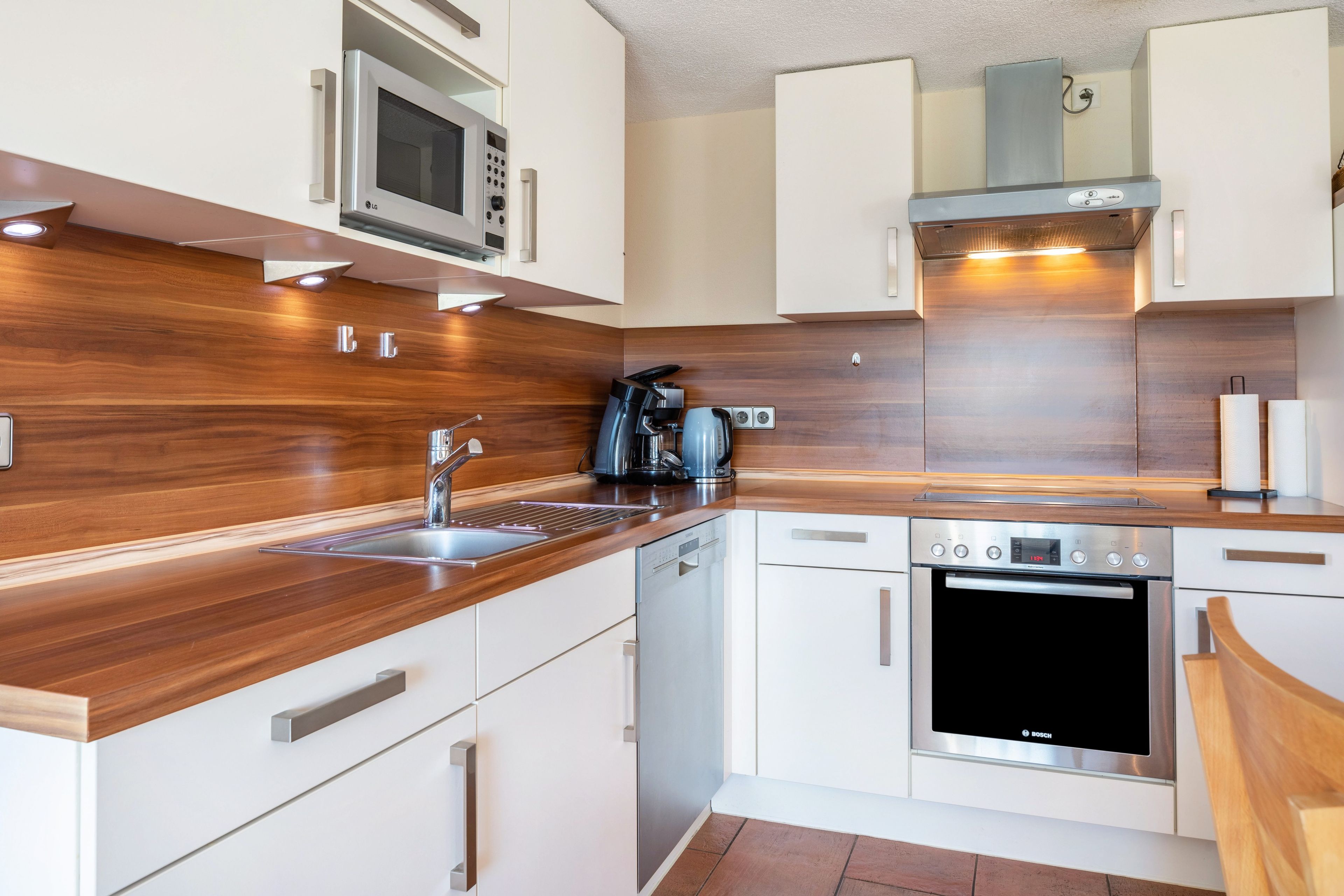 Een moderne keuken met witte kasten, roestvrijstalen apparatuur en een houten aanrecht.