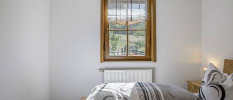 A bedroom with a bed, a window, a radiator, and a bedside table with a lamp.