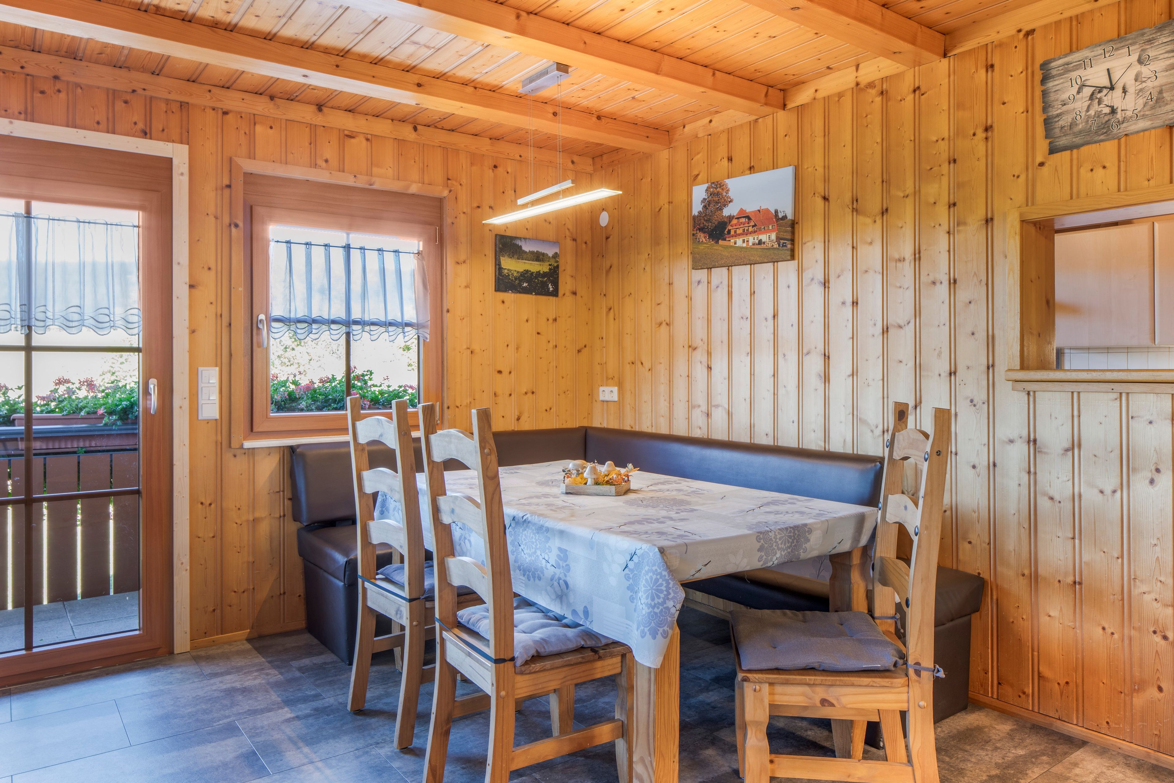 A wooden interior with a dining table set for four, surrounded by wooden chairs with cushions.