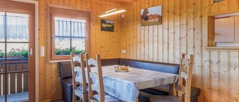 A wooden interior with a dining table set for four, surrounded by wooden chairs with cushions.
