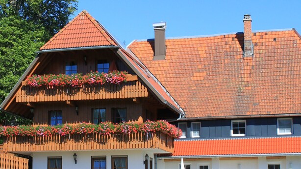 Un edificio de dos pisos con techo inclinado, balcones de madera con macetas de flores y un césped bien cuidado.
