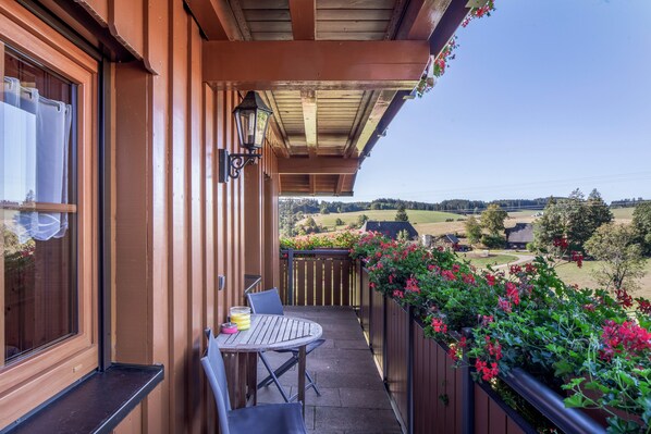 A wooden balcony with a table and chairs, overlooking a rural landscape with fields and houses. - Apartment 'Talaue' with Terrace, Barbecue Area, Playground and Countryside View (Sankt Georgen im Schwarzwald)