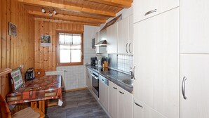 Una cocina con paneles de madera, armarios blancos, una mesa de comedor con un mantel individual y una ventana con persianas.