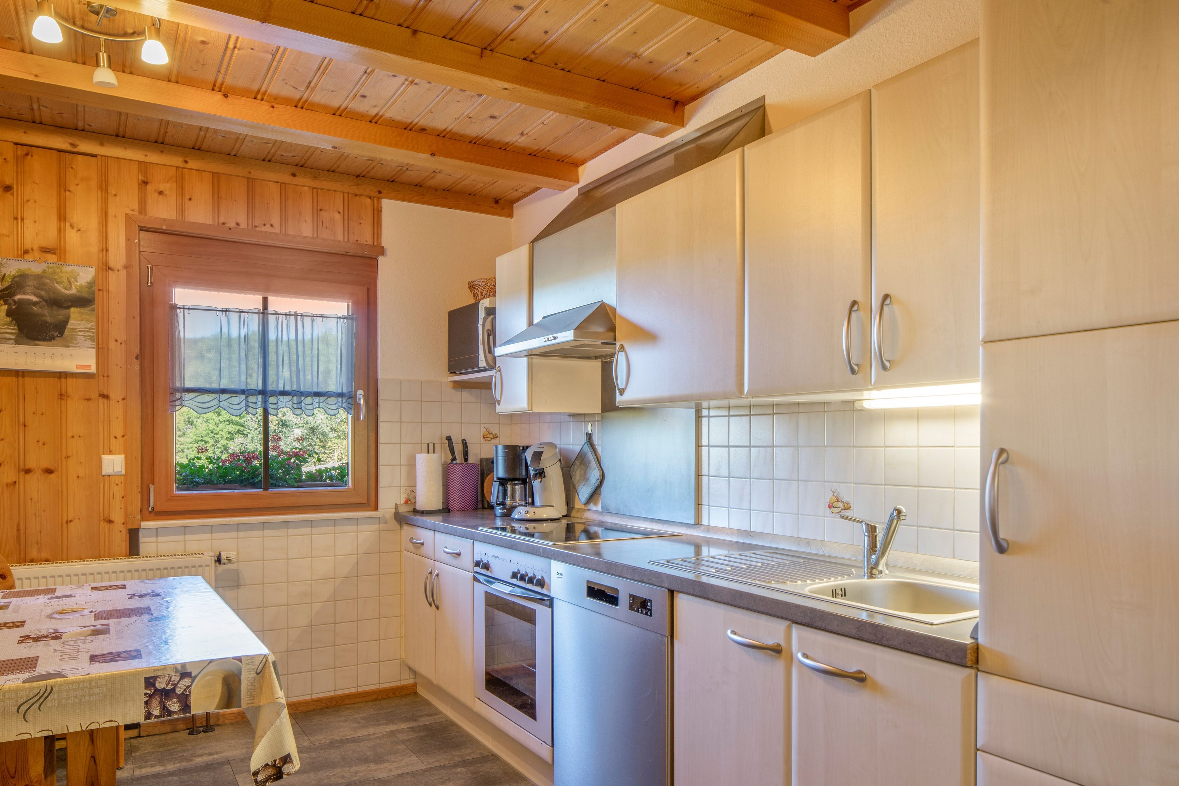 Eine Küche mit Holzbalken, einem Fenster mit Blick, einer Kaffeemaschine und Edelstahlgeräten.