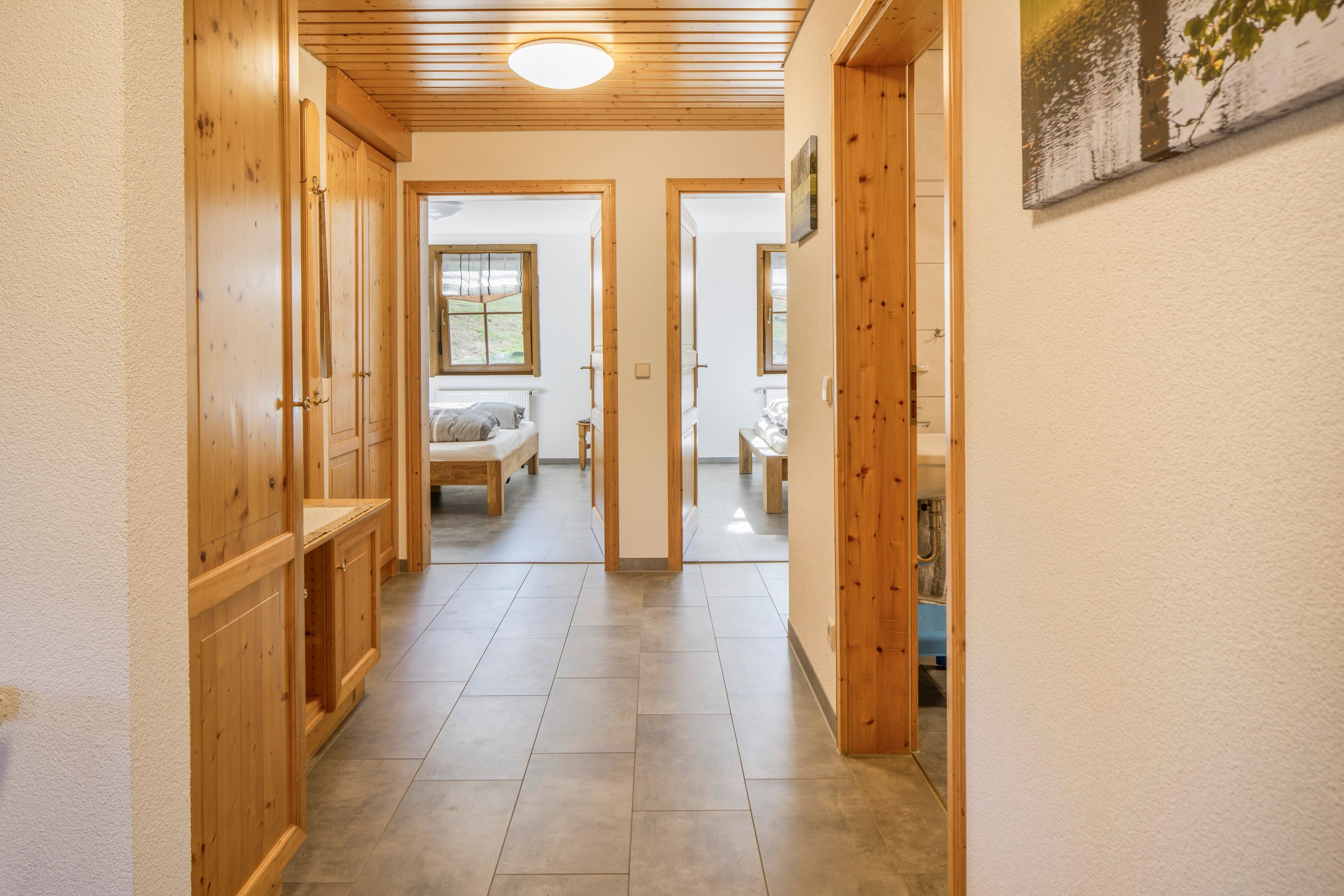 Ein Flur mit Holztüren und Fliesenboden, der zu einem Schlafzimmer mit Bett und Fenster führt.