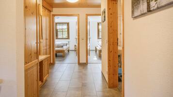 Ein Flur mit Holztüren und Fliesenboden, der zu einem Schlafzimmer mit Bett und Fenster führt.