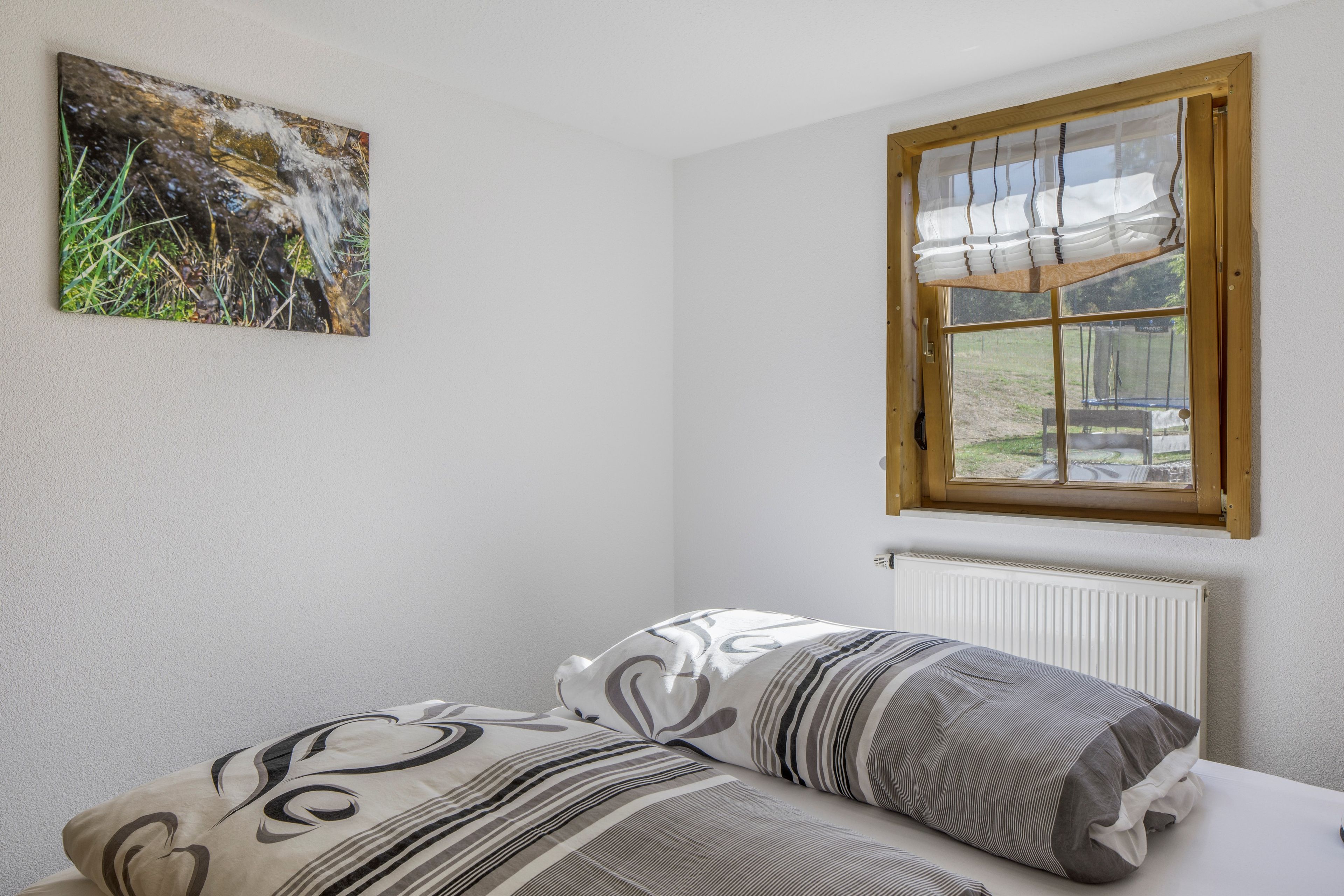A bedroom with a bed, a window, a radiator, and a wall-mounted picture.