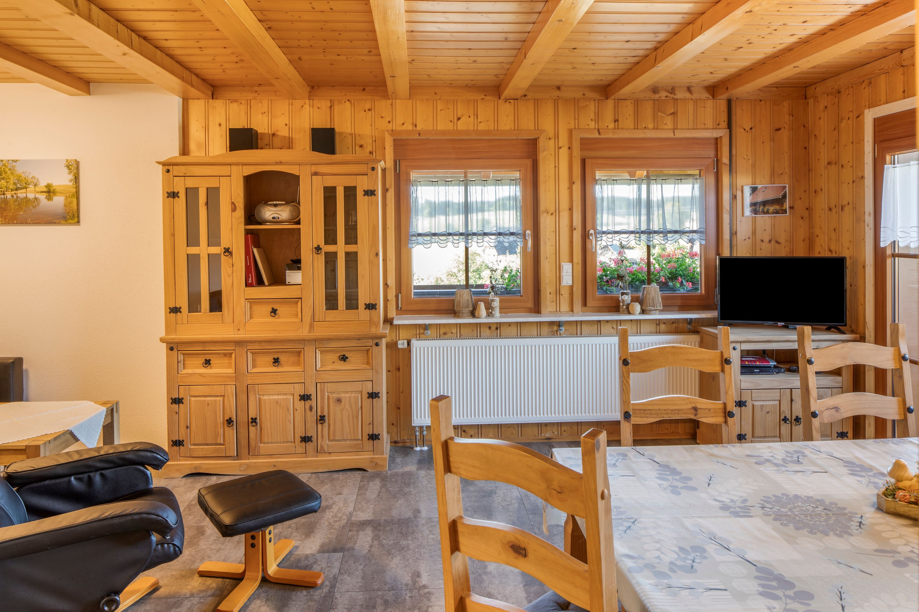 Ein Holzblock-Innenraum mit Esstisch, Stühlen, Fernseher und einer Vitrine.