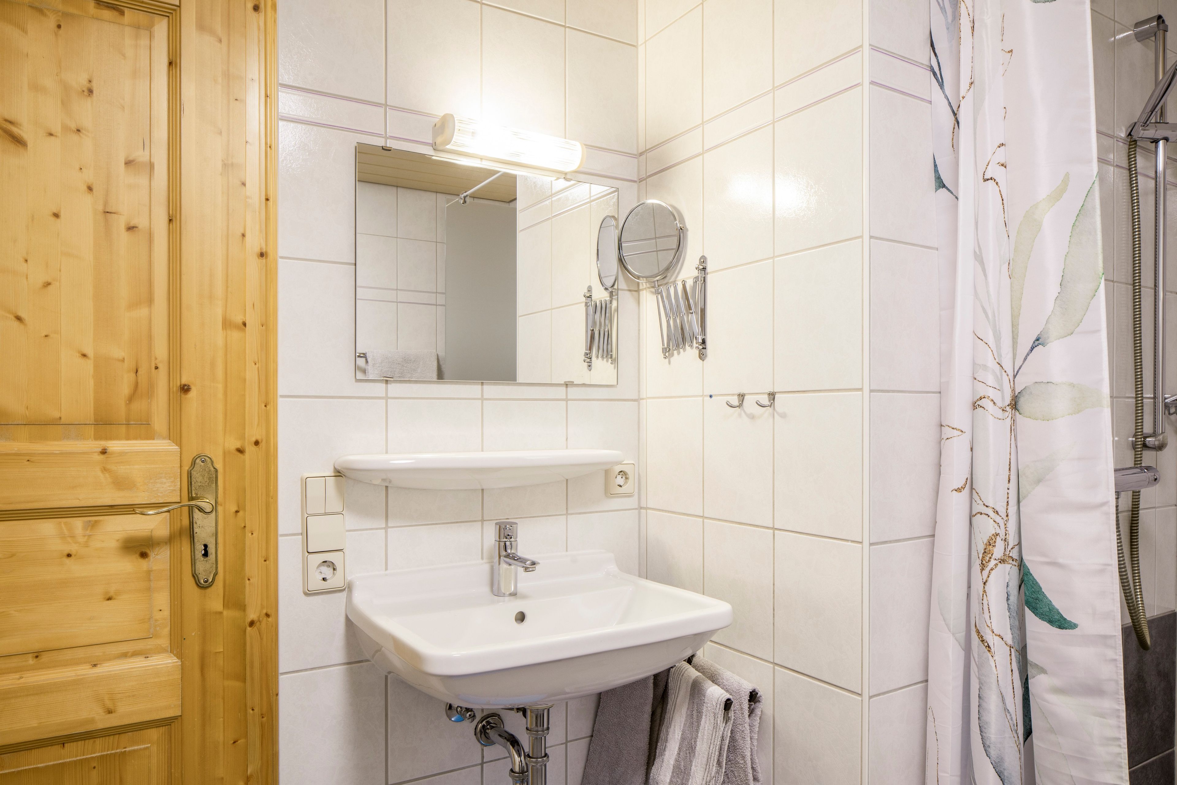 Un baño con puerta de madera, un lavabo blanco, un espejo y una cortina de ducha.