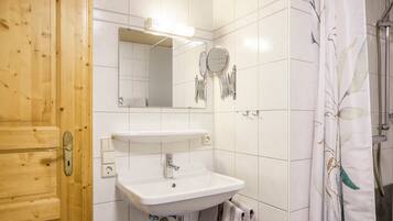 Un baño con puerta de madera, un lavabo blanco, un espejo y una cortina de ducha.