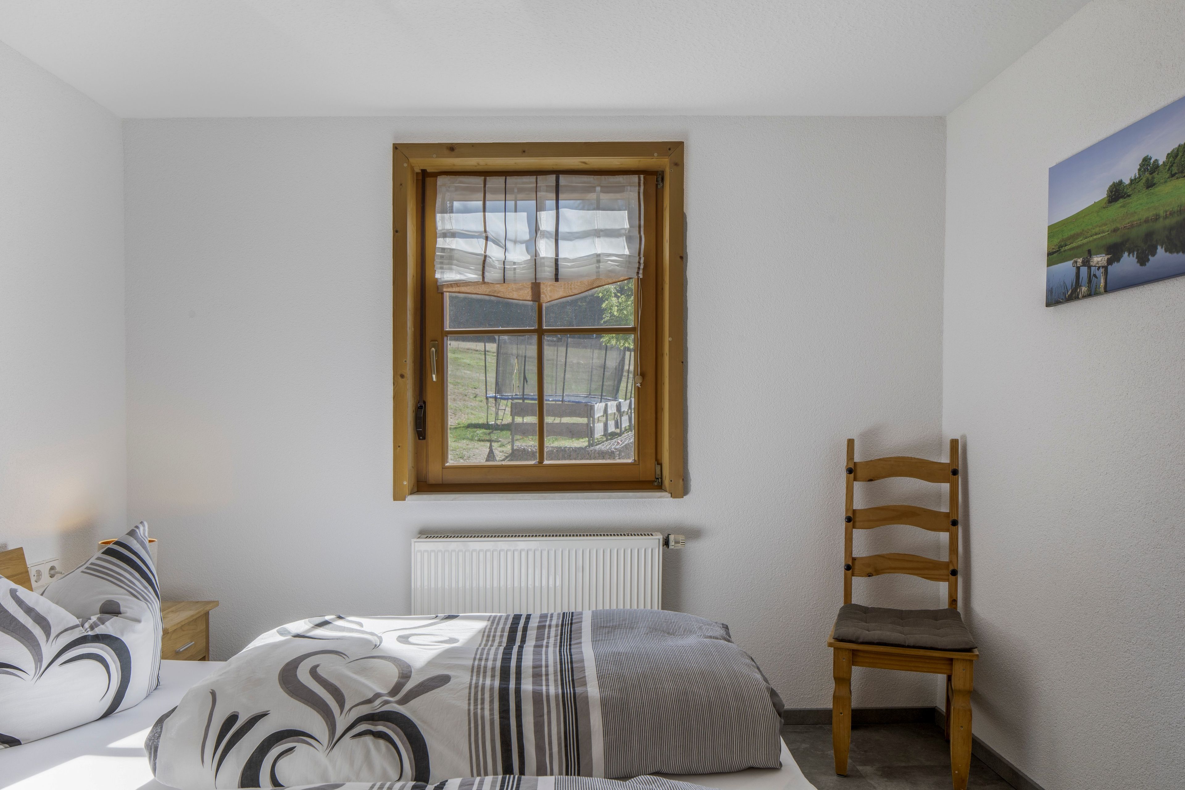 A bedroom with a bed, a chair, a radiator, and a window with a view of a landscape.