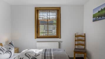 A bedroom with a bed, a chair, a radiator, and a window with a view of a landscape.