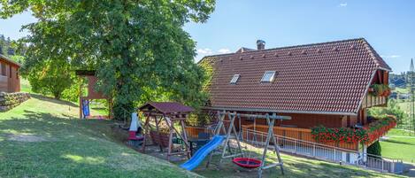 Il s’agit d’une propriété résidentielle dotée d’un grand arbre, d’un espace de jeux avec un toboggan et d’une maison avec un toit en tuiles.
