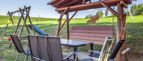 Ein hölzerner Pavillon mit Tisch und Stühlen, einer Schaukel und einer Rutsche in einem grünen Park.