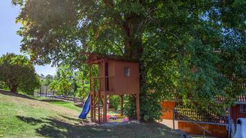 A wooden play structure with a slide, surrounded by trees and grass.