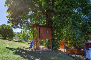A wooden play structure with a slide, surrounded by trees and grass. - Apartment 'Waldblick' on the farm with terrace, barbecue area, playground and green views (Sankt Georgen im Schwarzwald)