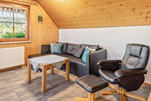 A cozy room with a wooden ceiling, a sofa with cushions, a leather chair, and a small table with a cloth. - Apartment 'Waldblick' on the farm with terrace, barbecue area, playground and green views (Sankt Georgen im Schwarzwald)