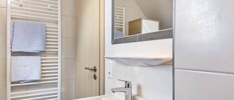 Un baño con un lavabo blanco, un espejo y un perchero con dos toallas.