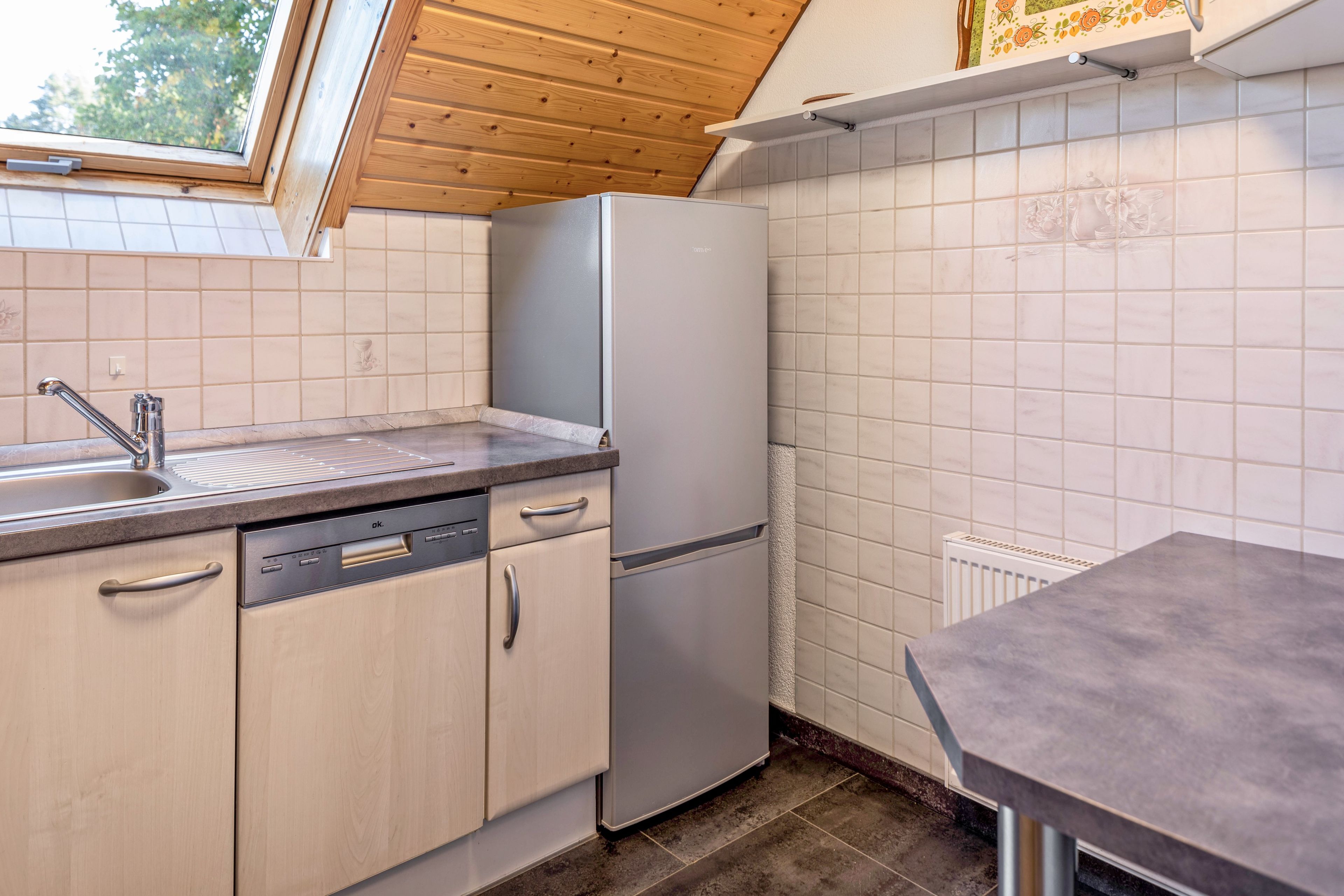 A compact kitchen with a built-in dishwasher, a refrigerator, and a window above the sink.